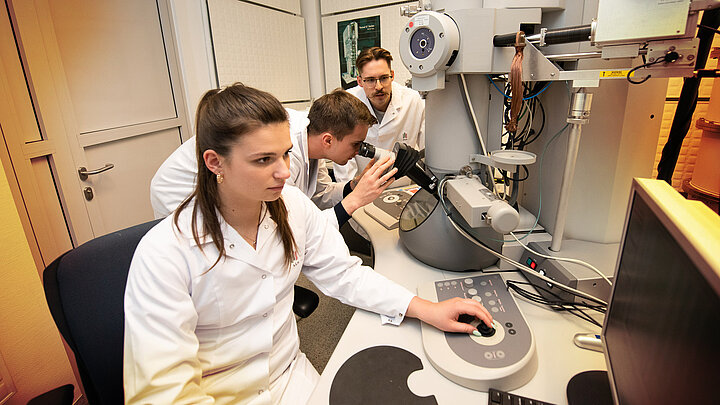 Troje naukowców pracyjących przy nowoczesnym mkkroskopie elektronowym.